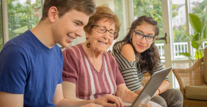 Young Adults sitting with elderly lady on couch on computer donating to Charles E. Smith Life Communities