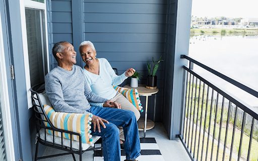 An older couple sitting on a balcony overlooking a lake.